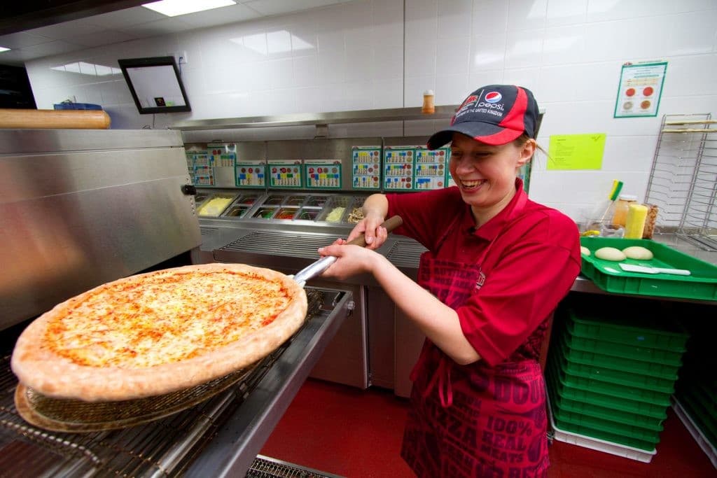 Papa Johns team member taking a pizza from the oven